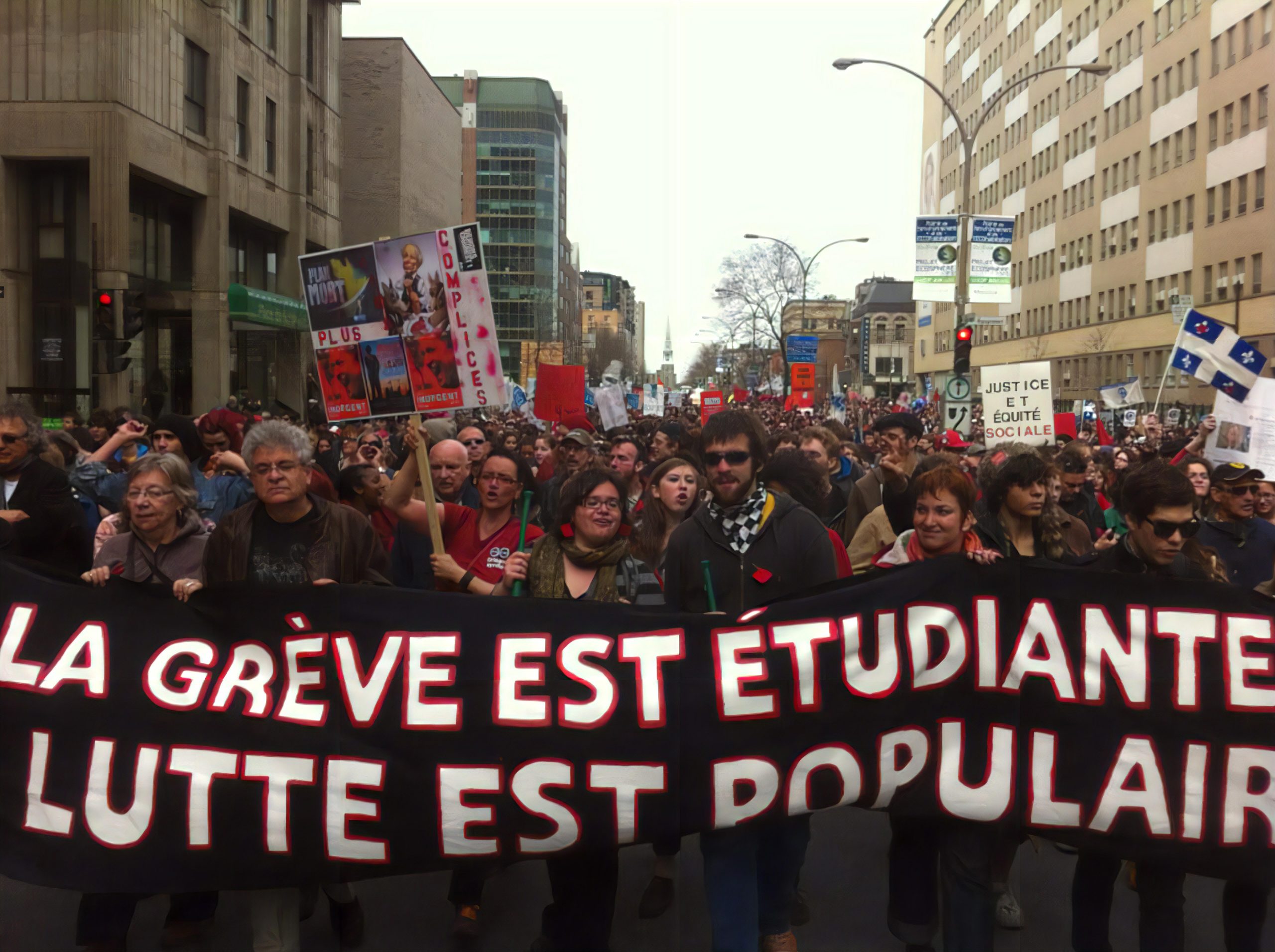 image of a large group of people protesting in a Montreal street with a big banner that reads "La Grève est Étudiante Lutte est Populaire"