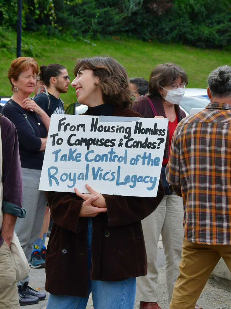 Person holding a sign that reads "From Housing Homeless to Campuses and Condos? Take Control of the Royal Vic's Legacy