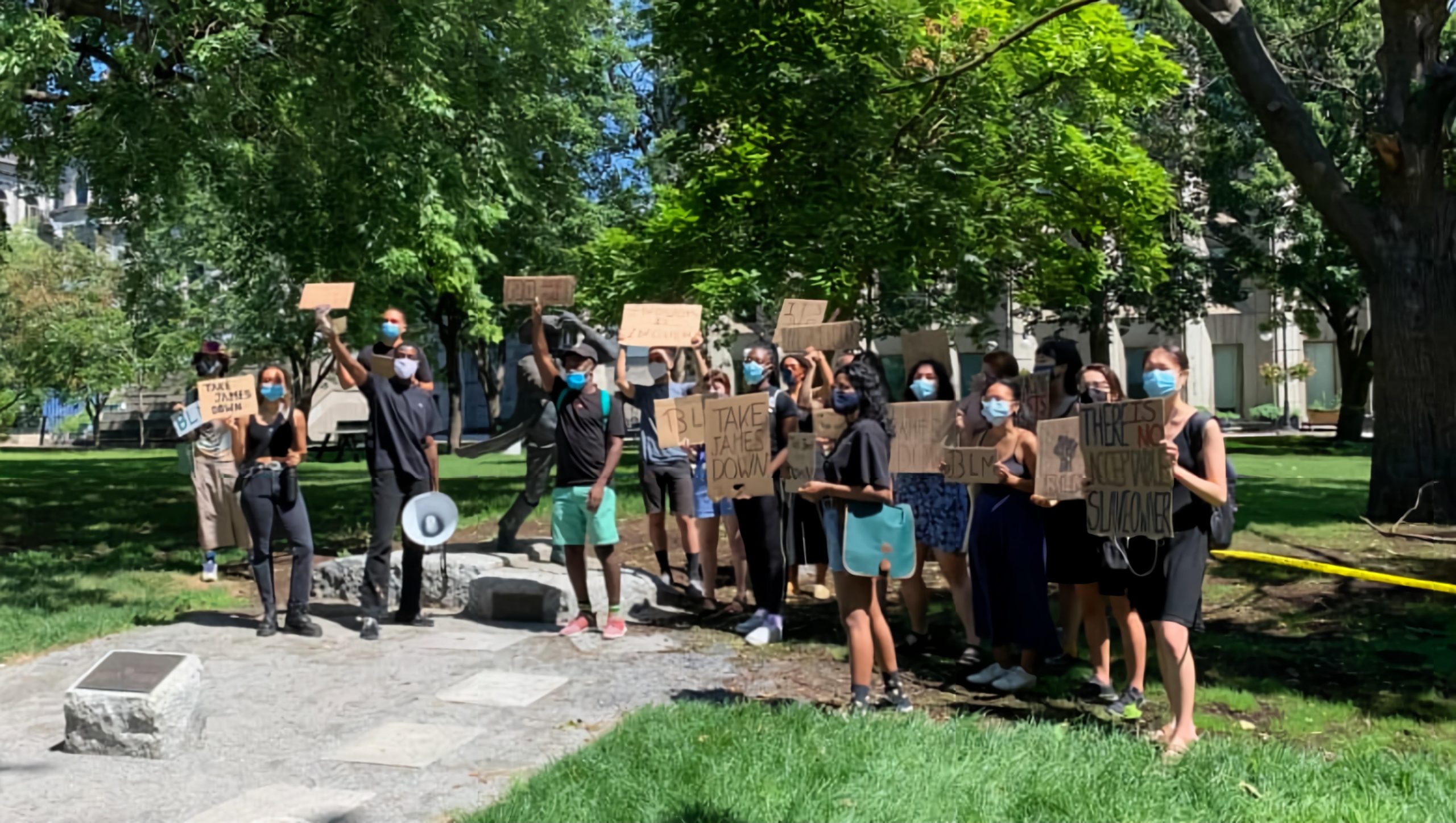 Group of predominantly black people standing in front of the James McGill statue holding signs